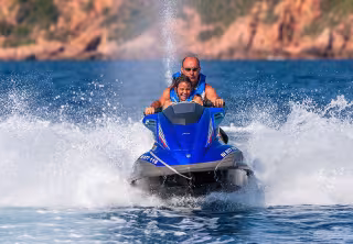 Couple sur un jet ski lancé à pleine vitesse dans une gerbe d'eau, rochers rouges en arrière-plan