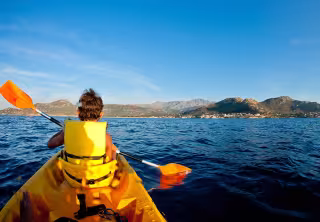 Kayakiste en gilet de sauvetage pagayant en mer, face à la côte et aux montagnes