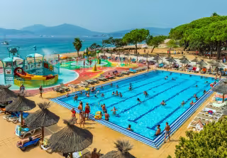 Piscine et parc aquatique au bord de la plage, entourés de parasols en paille