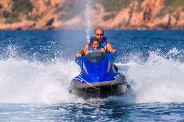 Couple sur un jet ski lancé à pleine vitesse dans une gerbe d'eau, rochers rouges en arrière-plan